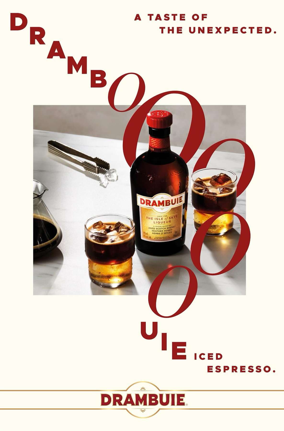 Bottle of Drambuie liqueur on a marble surface with two glasses of iced espresso and bar tongs, next to red Drambuie lettering.