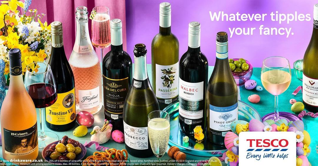 Assortment of wine bottles and glasses alongside Easter decorations and snacks, set against a purple backdrop in a promotional display.