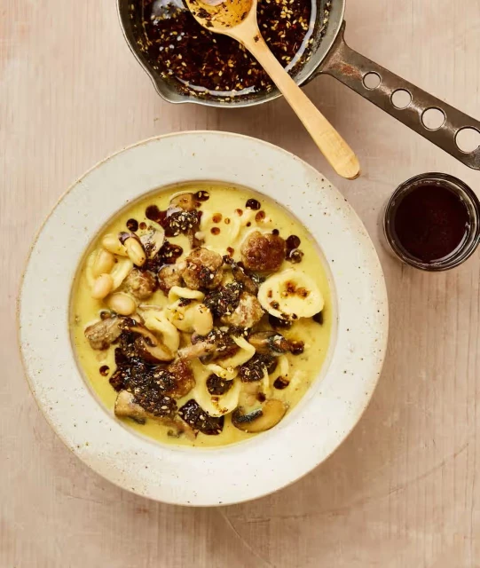 Overhead view of orecchiette pasta with mushrooms and white beans in creamy yellow sauce, drizzled with dark balsamic glaze.