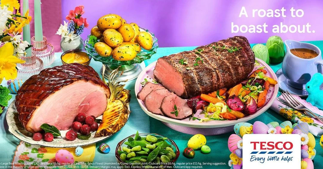 A colorful Easter-themed food still life with a ham, roast beef, potatoes, vegetables, and Easter decorations on a light blue tablecloth.