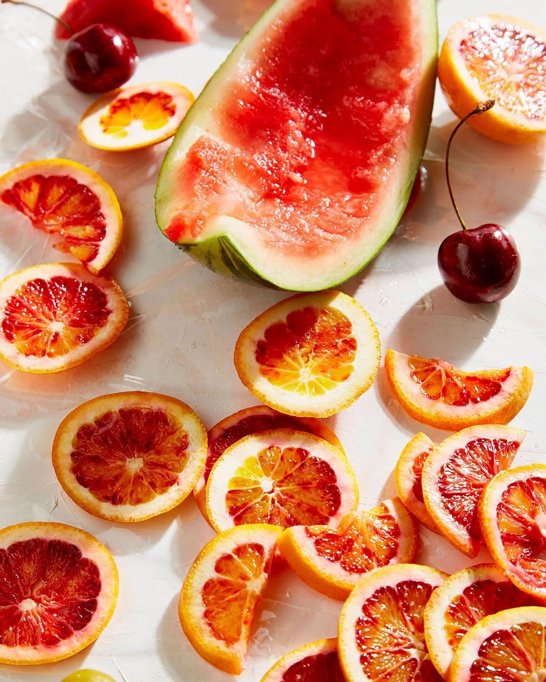 Overhead still life shot featuring a vibrant array of sliced blood oranges, cherries, and watermelon, creating a colourful display of fresh fruit.