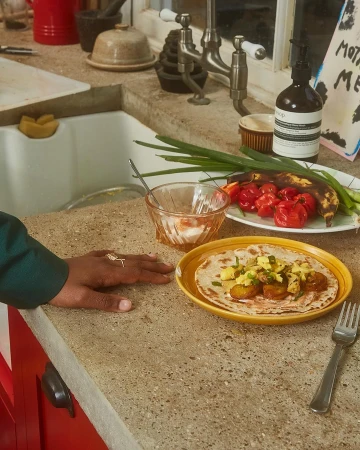 Overhead shot of a tortilla on a yellow plate, topped with potatoes, eggs, and green onions, alongside fresh peppers on a kitchen counter.