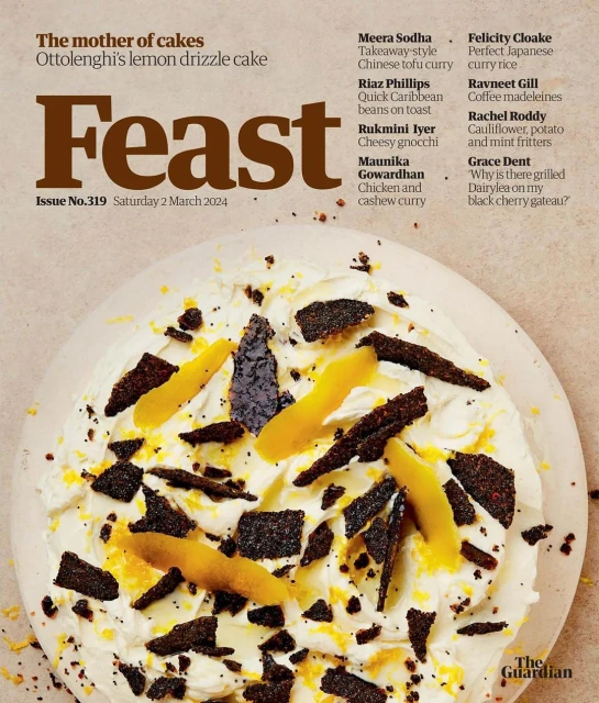 Overhead close-up of a 'Feast' magazine cover featuring a decorated lemon cake with icing, zest, and dark candied elements.