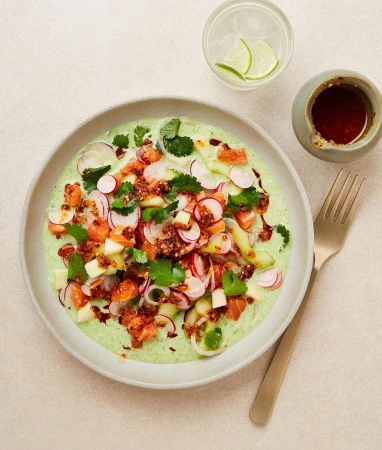 Overhead shot of a light green plate containing salmon with radishes, apples, and herbs, accompanied by a golden fork and condiments.