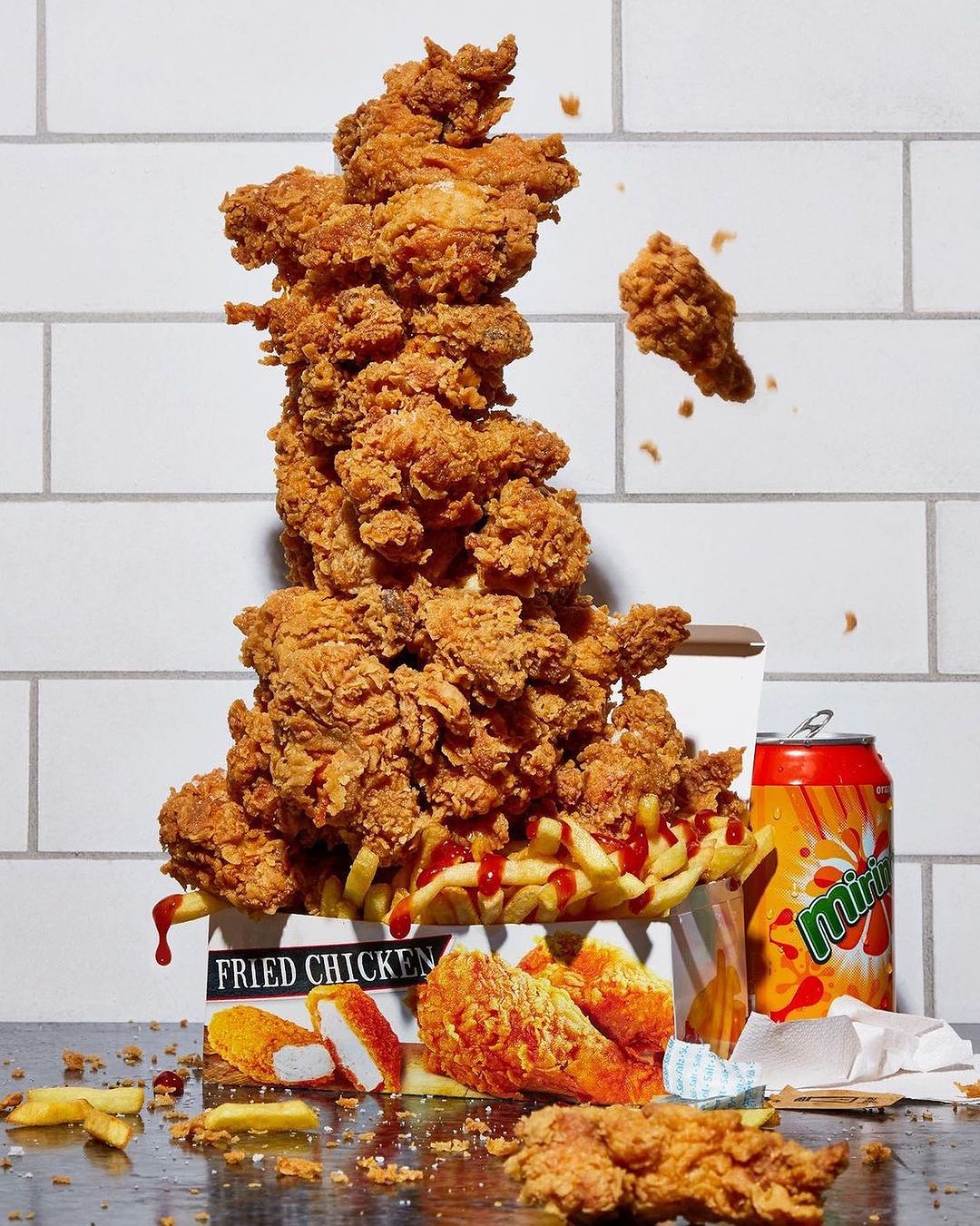 Tower of fried chicken wings and french fries stacked on a box with a soda can, showcasing a culinary indulgence.