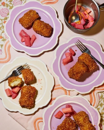 Overhead shot of four plates of golden-brown fried food, garnished with pink vegetables, set on a floral tablecloth with a metal pot.