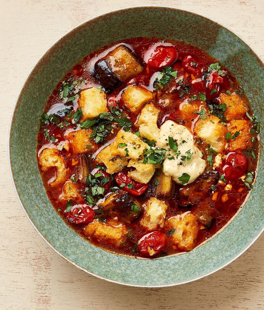 Overhead shot of a bowl of pappa al pomodoro featuring bread, tomatoes, herbs, eggplant, and a creamy sauce, presented on a table.