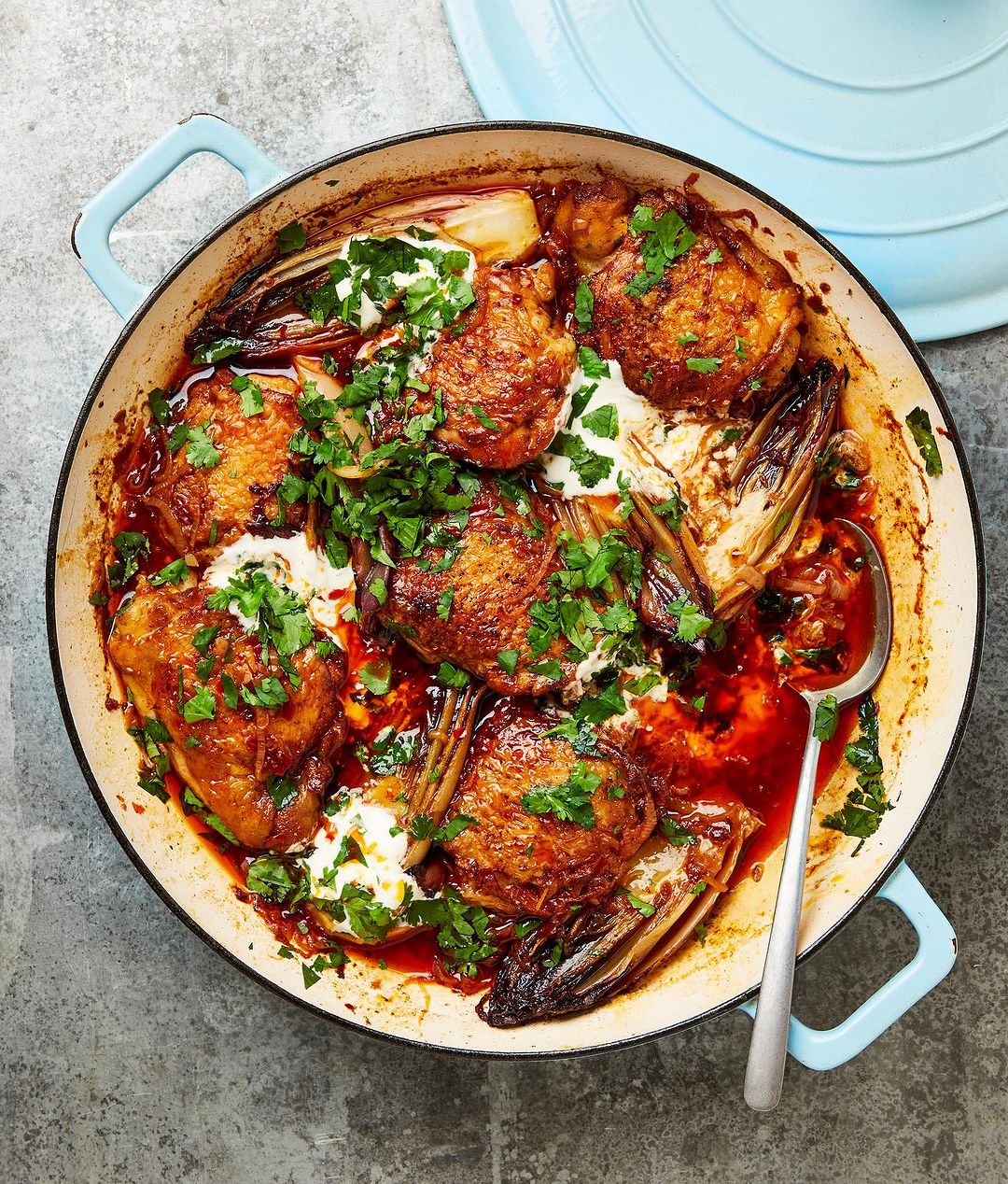 Overhead shot of a light blue pan filled with roasted chicken thighs, endives, fresh herbs, and a creamy white sauce.