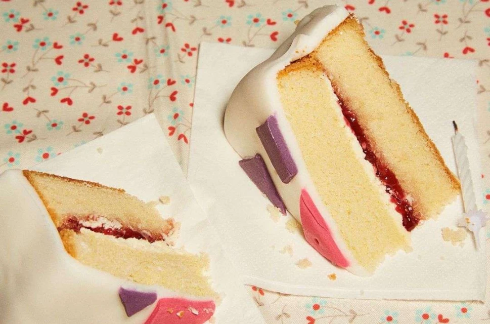 Two slices of birthday cake with white frosting, decorated with colorful shapes and strawberry filling, sitting on paper napkins.
