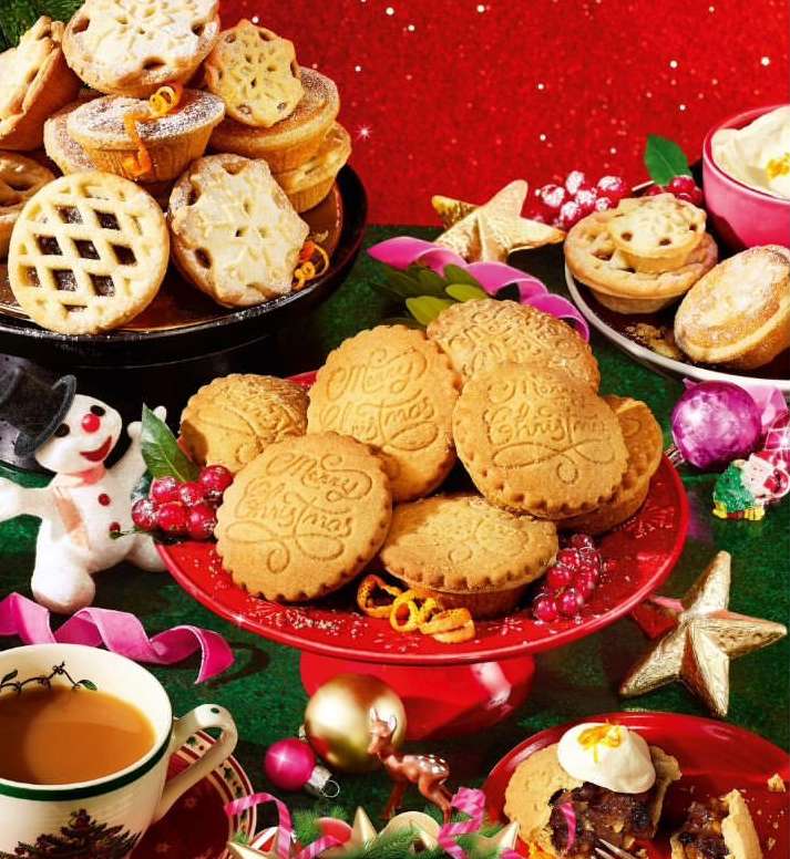 Festive holiday display with an assortment of desserts including mince pies and cookies, set against a red and green background.