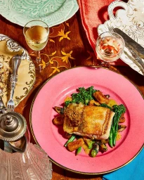 Pan-seared fish fillet with broccolini on a pink plate on a wooden table shot from above by Louise Hagger.