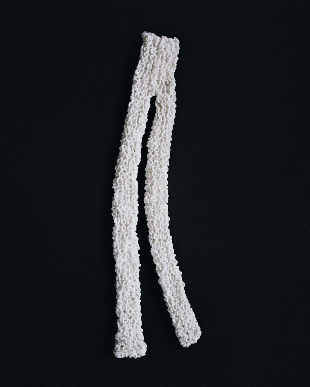 Textured white textile on black background. Abstract soft material arranged vertically in two strands for fashion, art, design.