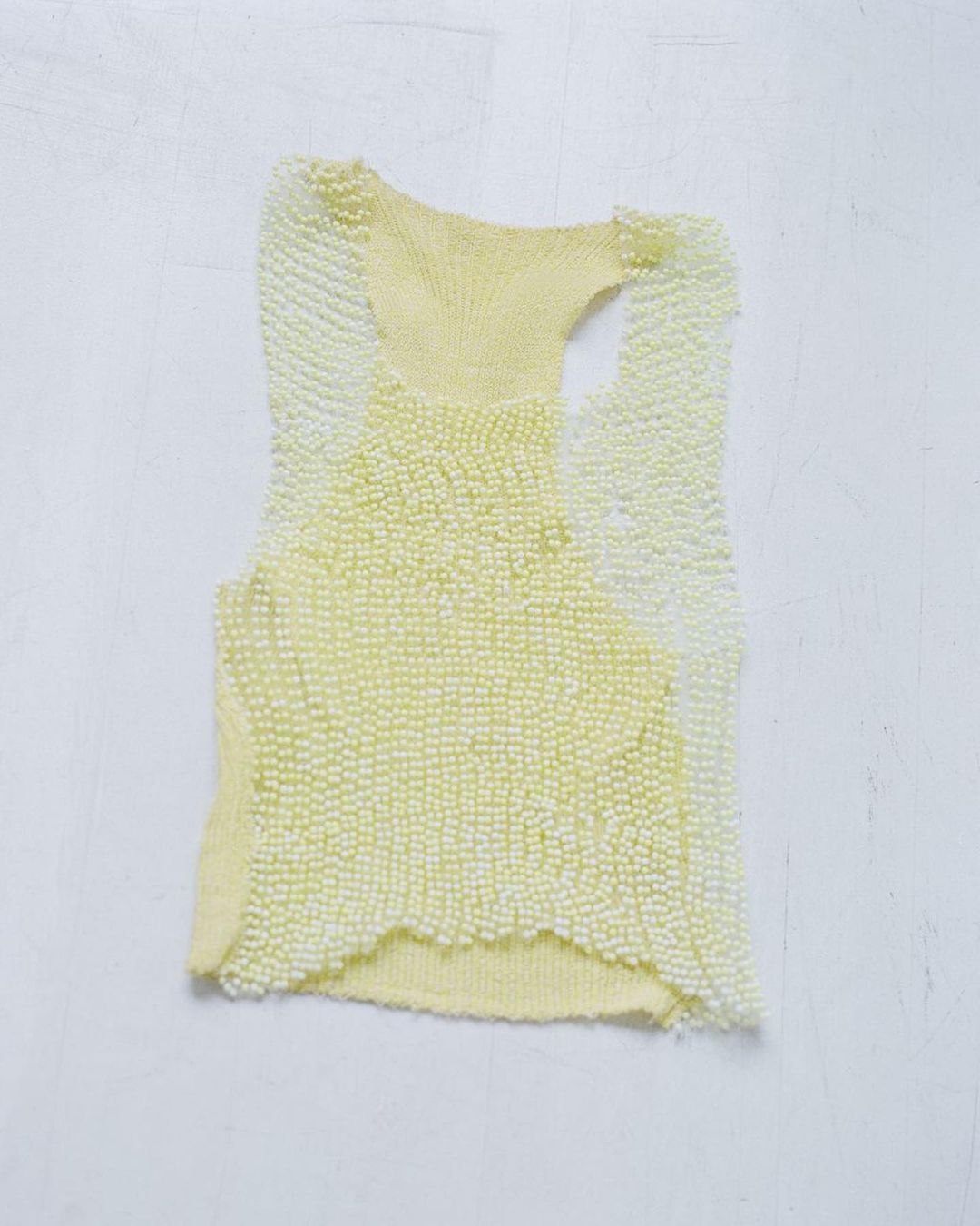 Abstract studio shot of a textured light-yellow tank top against a white background creating a minimalist, visually appealing fashion image.