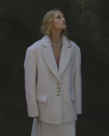 Model in a cream fuzzy textured blazer and necklace looking up outdoors by Luba Kozorezova