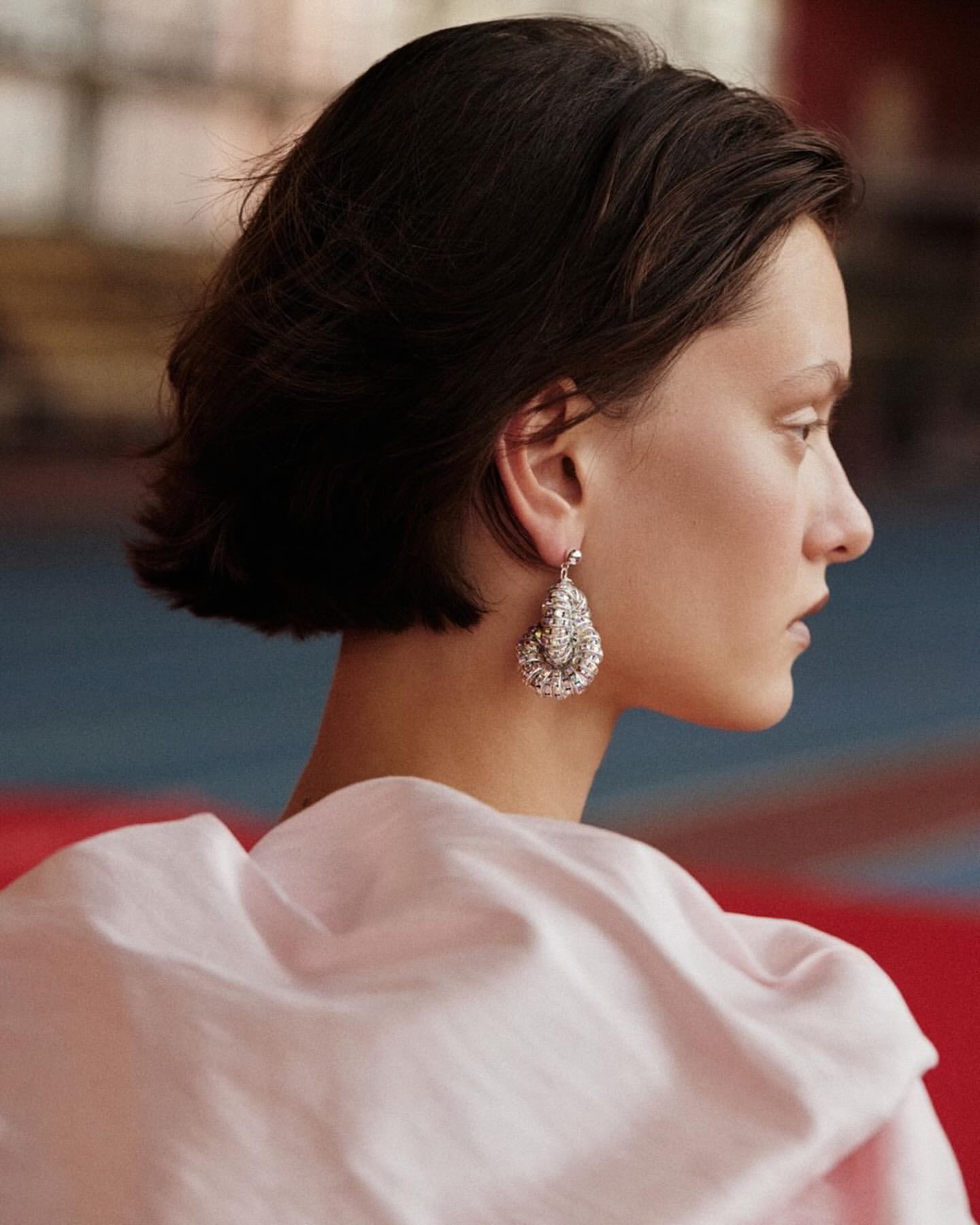 Profile portrait of a woman with dark short hair wearing an ornate silver dangling earring and a pale pink draped garment.