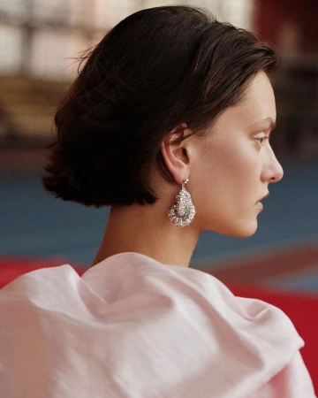 Profile portrait of a woman with dark short hair wearing an ornate silver dangling earring and a pale pink draped garment.