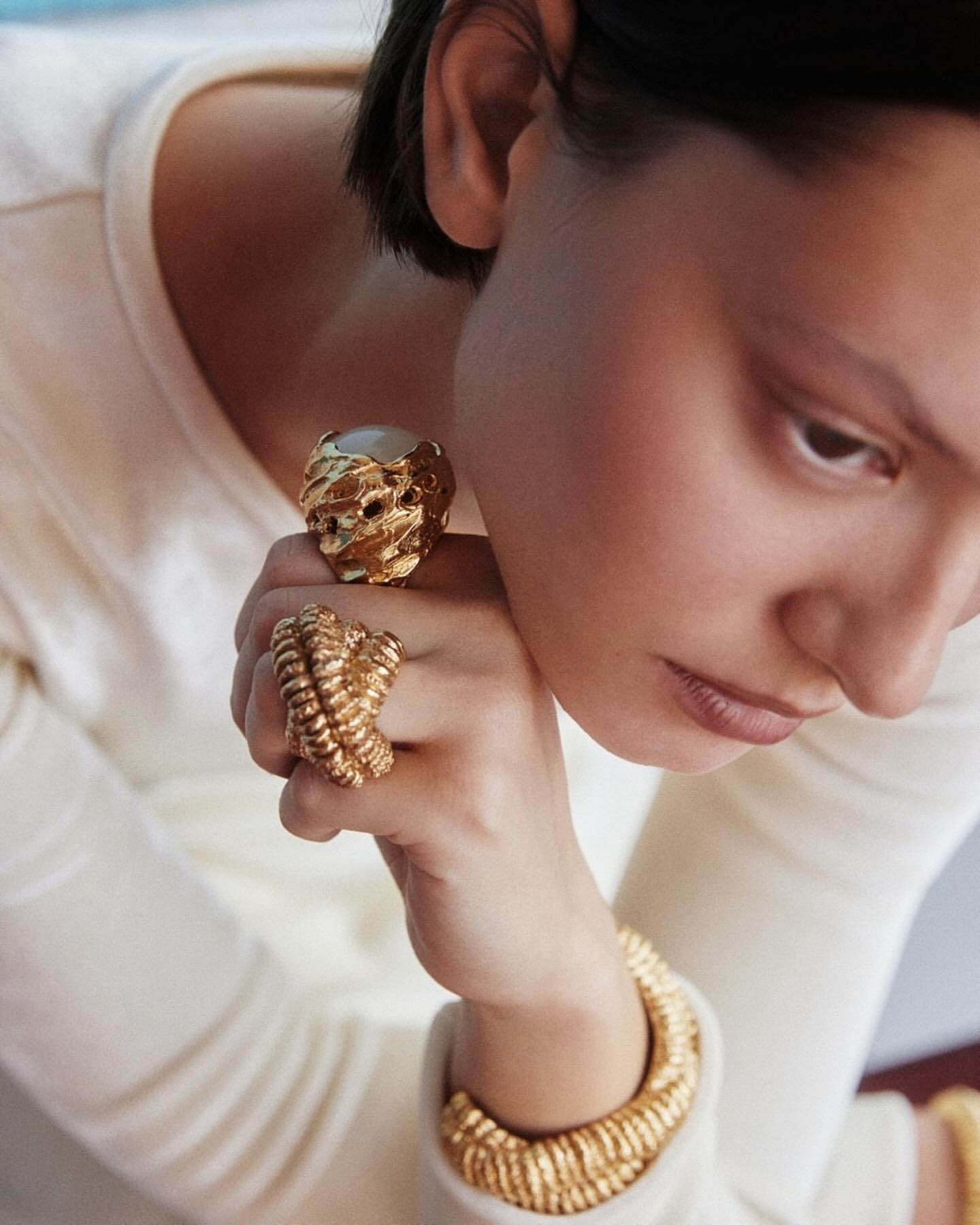 Close-up of a light-skinned woman showcasing golden rings and a matching bracelet, set against a clean, neutral background.