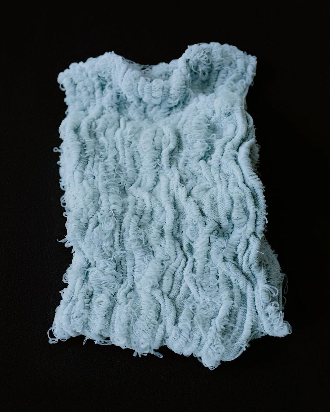 Close-up of a light blue, textured newborn photography prop on a black background, showcasing its delicate ruffles and patterns.