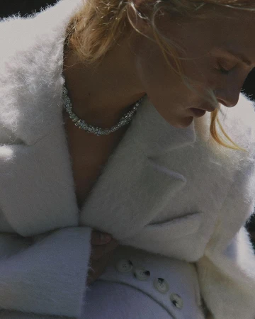 Close-up portrait of a woman wearing a fluffy white textured coat and a sparkling rhinestone necklace.