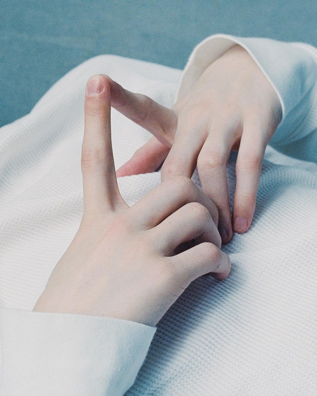 Close-up photo of two fair-skinned hands against an off-white textured surface, one with a single finger raised in a gesture.