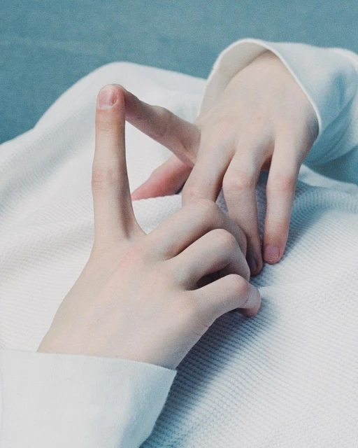 Close-up photo of two fair-skinned hands against an off-white textured surface, one with a single finger raised in a gesture.