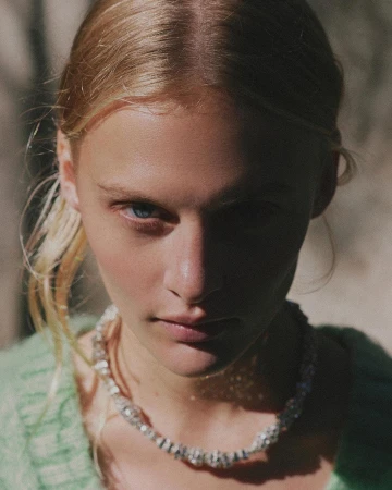 Close-up portrait of a woman wearing a green knitted sweater and a sparkling necklace in natural light