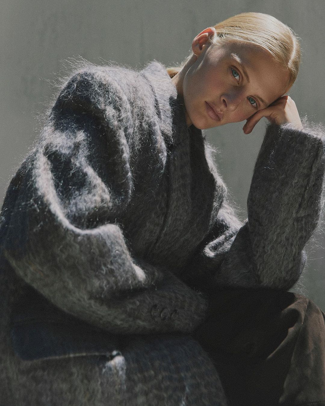 A young adult woman poses in a grey, textured coat. The portrait showcases a serene expression and soft, diffused lighting.