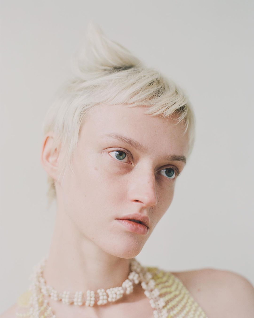 Portrait of a blonde woman wearing a beaded necklace against a plain neutral background by Luba Kozorezova in Paris.