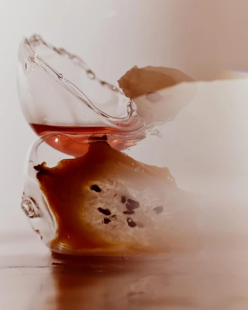 A glass with liquid splashes upwards, with a sliced fruit inside, against a gradient cream to white background, food and beverage photography.