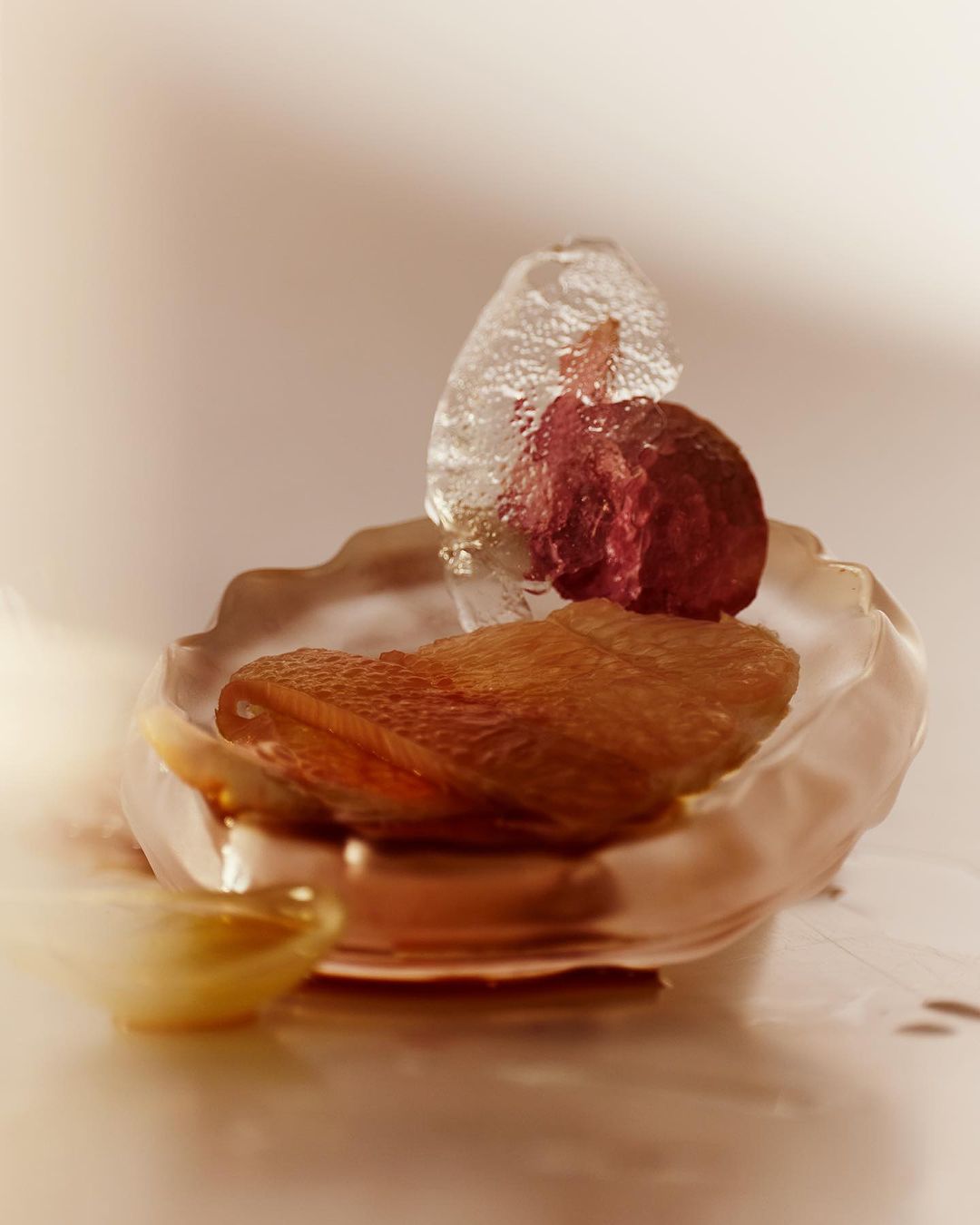 Still life with a dessert, a glass dish, ice, and a red fruit, shot in a photo studio with neutral tones and soft lighting.