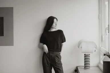 Monochrome portrait of a woman leaning against a wall indoors next to a striped lamp, shot by Luba Kozorezova.