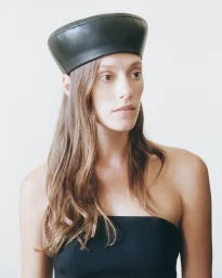 Woman wearing a black leather beret and strapless black top against a plain light background
