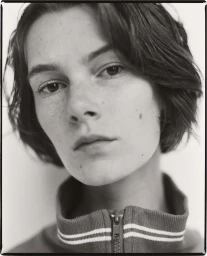Close-up portrait of a young woman with dark short hair and freckles wearing a zipped collar top by Luba Kozorezova in Paris