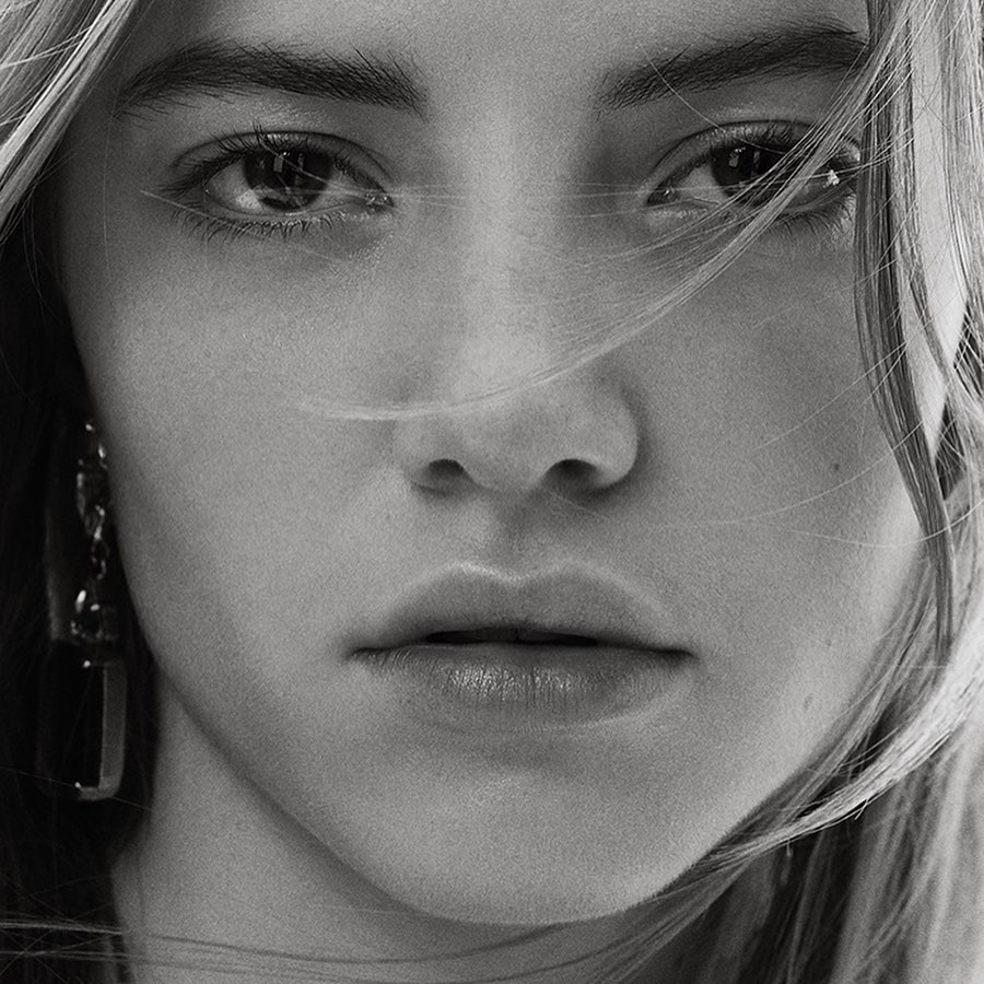 Close-up black and white portrait of a woman's face with strands of hair blowing across her eyes.
