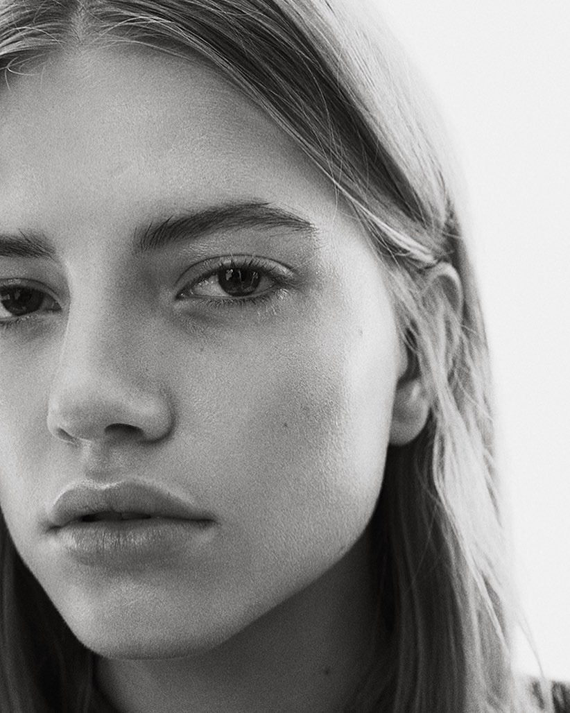 Close-up monochrome portrait of a young woman with a serious expression and straight blonde hair against a plain white background.