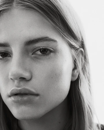 Close-up monochrome portrait of a young woman with a serious expression and straight blonde hair against a plain white background.
