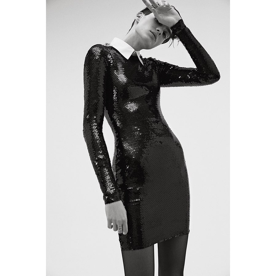 Monochrome shot of a fashionable adult woman with short hair wearing a sparkling black long-sleeved dress with a white collar.