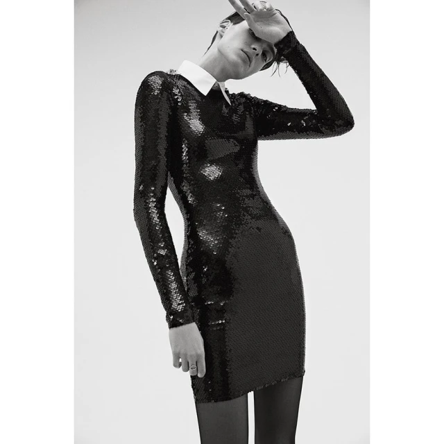 Monochrome shot of a fashionable adult woman with short hair wearing a sparkling black long-sleeved dress with a white collar.