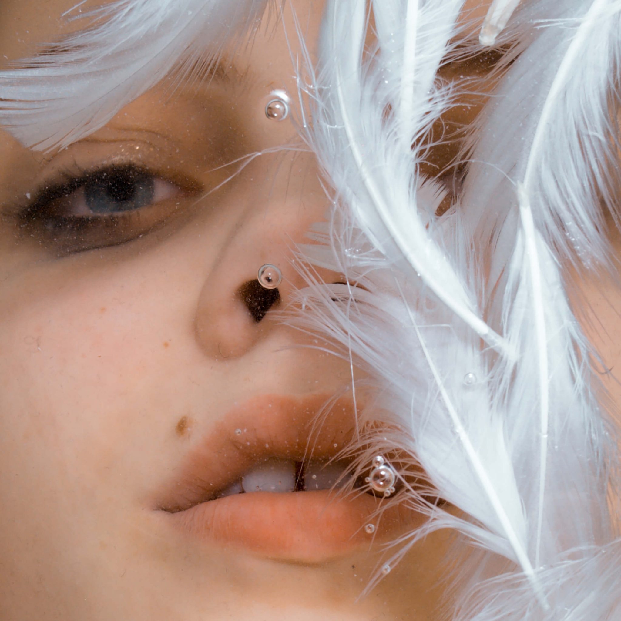 Close-up portrait of a young adult female partially submerged in water, surrounded by white feathers and small air bubbles.