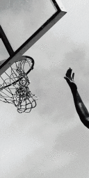 Monochrome vertical shot showing a raised arm reaching towards a basketball hoop and net outdoors.