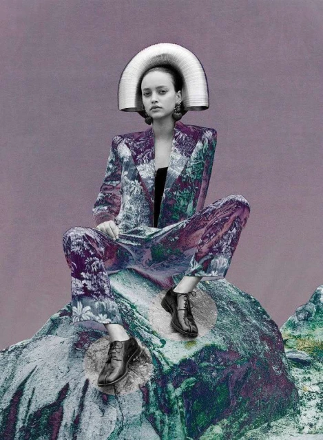 A woman sits on a rock wearing a floral-patterned suit and a large metal headdress. She has a neutral expression and is looking forward.