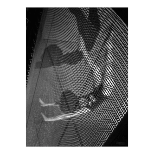 Black and white photo of two people's shadows reflected on a glass surface with a mesh pattern overlay in an indoor setting.
