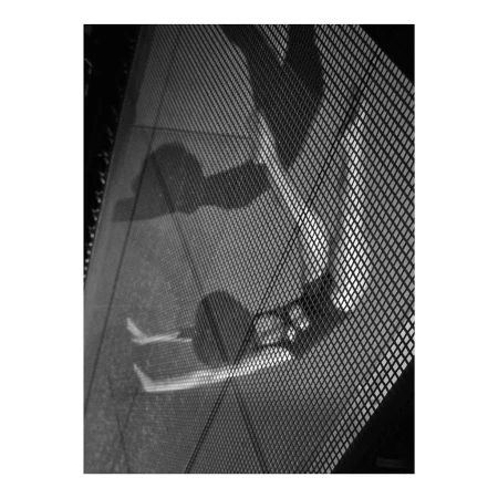 Black and white photo of two people's shadows reflected on a glass surface with a mesh pattern overlay in an indoor setting.