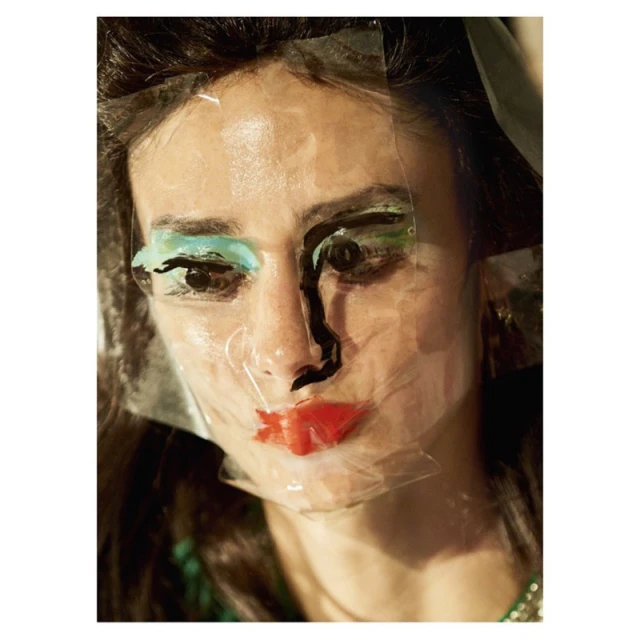 Close-up portrait of an adult female with red lipstick and blue eye shadow, partially covered by a sheet of clear plastic.