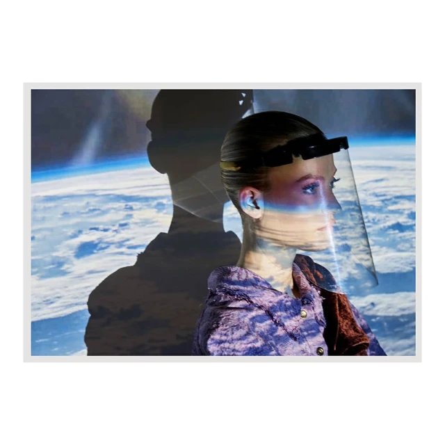 Woman with face shield stands in front of Earth projection, wearing a lavender textured jacket with a brown velvet lapel in a studio.