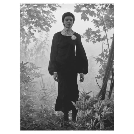 Model standing among misty trees wearing a long black dress with a high collar and floral lapel pin by photographer Lucian Bor