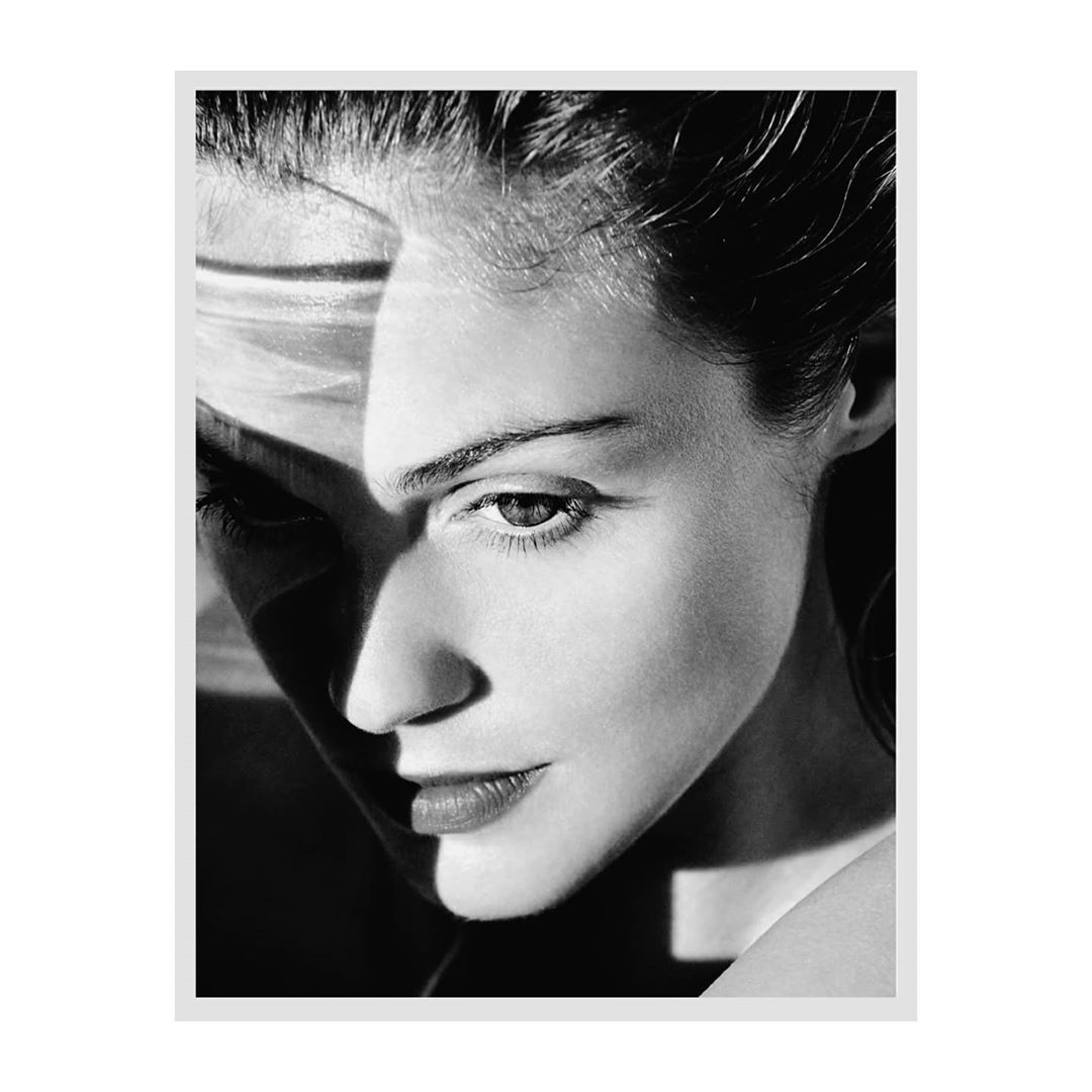 Close-up black and white portrait of a woman with dramatic harsh light casting diagonal shadows across her face by Lucian Bor in Paris.