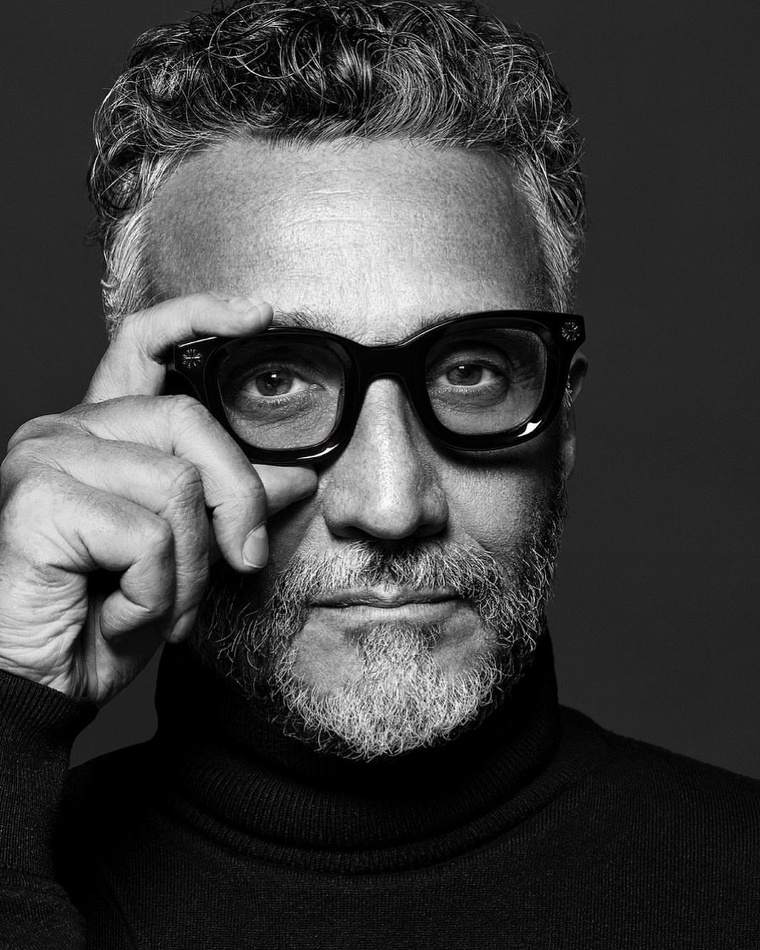 Black and white portrait of a mature adult man with gray hair and beard, wearing glasses and a turtleneck sweater.