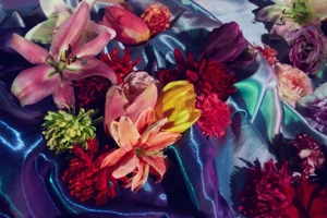 Colorful assortment of fresh flowers resting on shiny draped blue and purple satin fabric