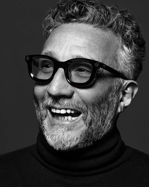 Monochrome portrait of a middle-aged man wearing thick black framed glasses and a dark turtleneck sweater.